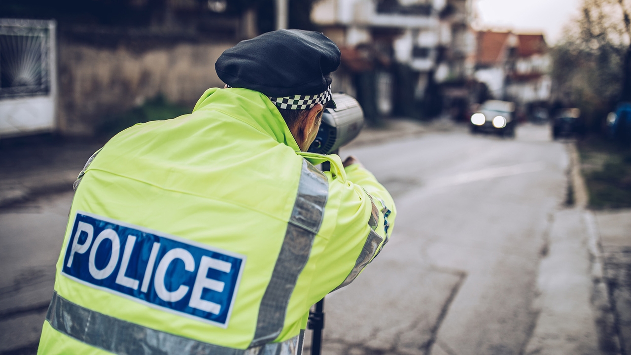 A police officer aims a handheld speed camera at a blurry car in the distance