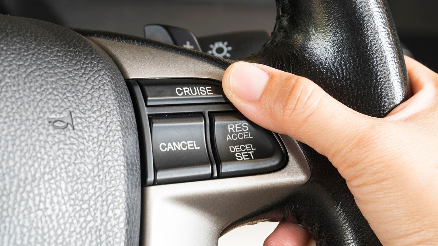 driver pressing cruise control button on steering wheel