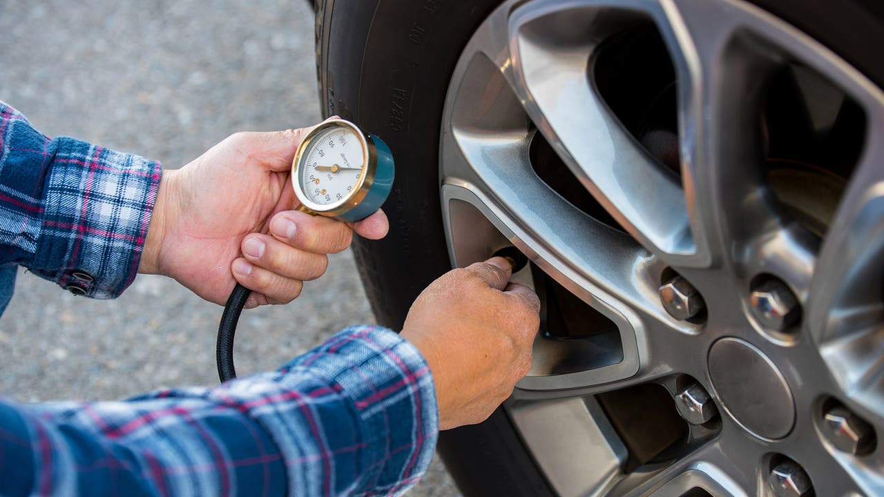 Driver checking a tyre's pressure with a gauge.