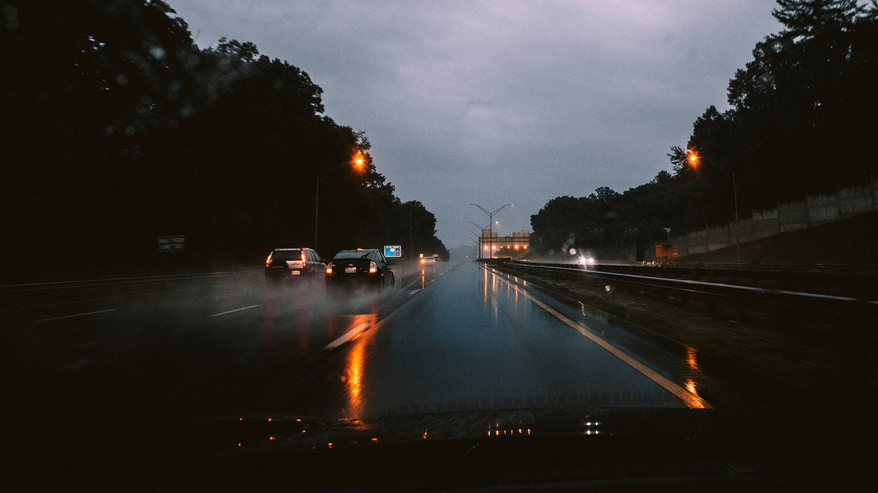 A car drives fast in the outside lane of the motorway overtaking two other cars in very wet conditions