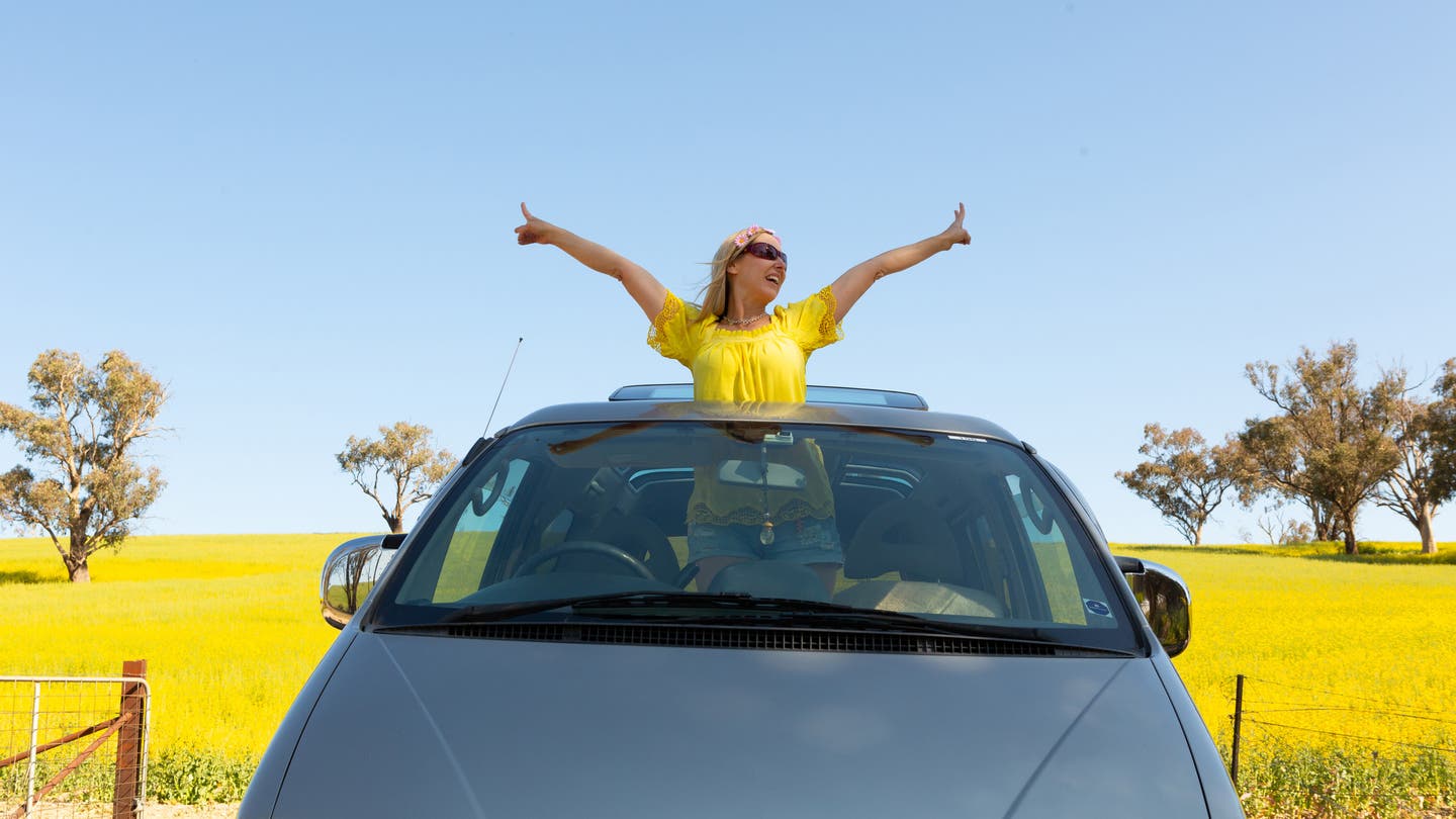 lady in yellow top with arms outstretched standing through sunroof