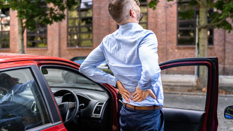 Man with back pain standing next to car