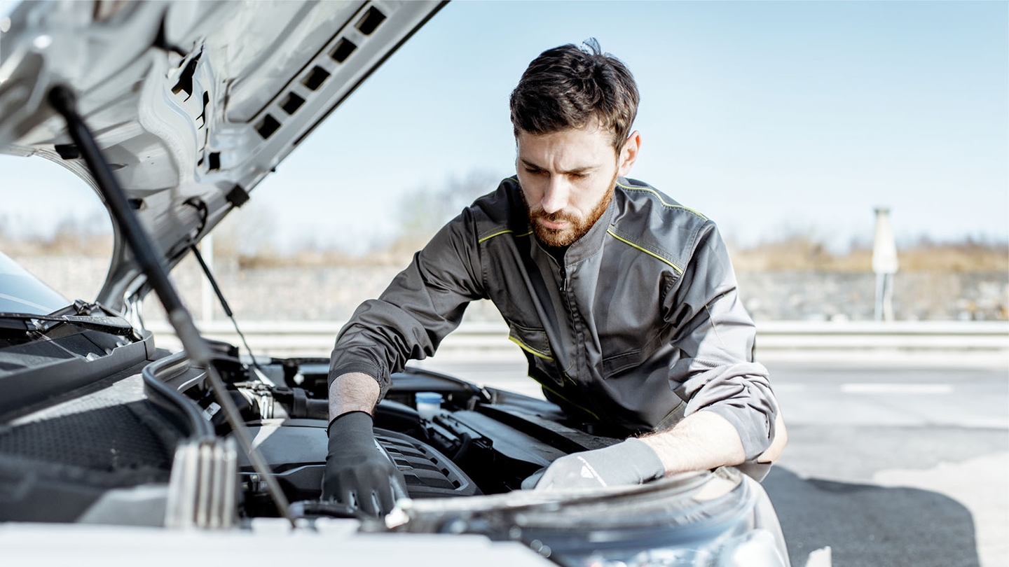 A mechanic in grey overalls works under the bonnet of a van