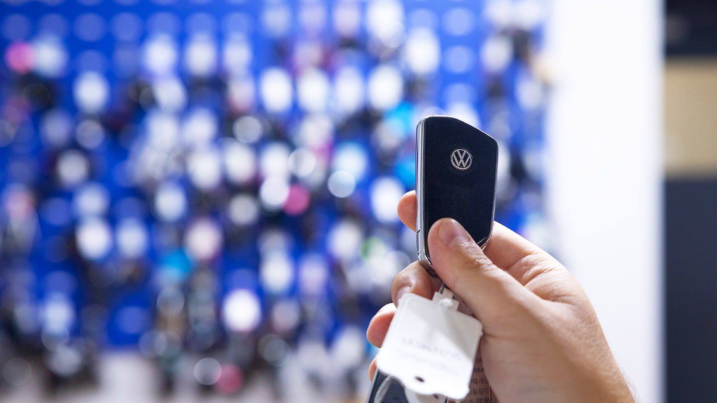 Volkswagen car key held up in front of blurry key board containing hundreds of other car keys