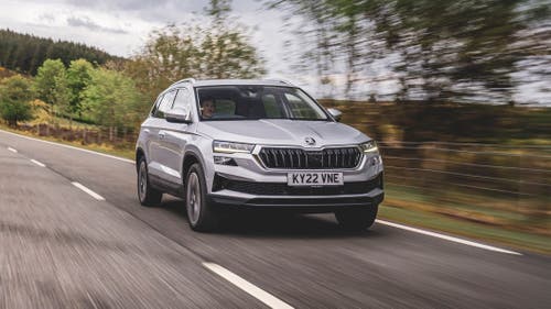 A silver Skoda Karoq drives through the English countryside