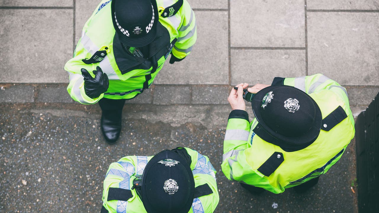 Three UK police officers in high-vis have a serious conversation, shot artistically from overhead