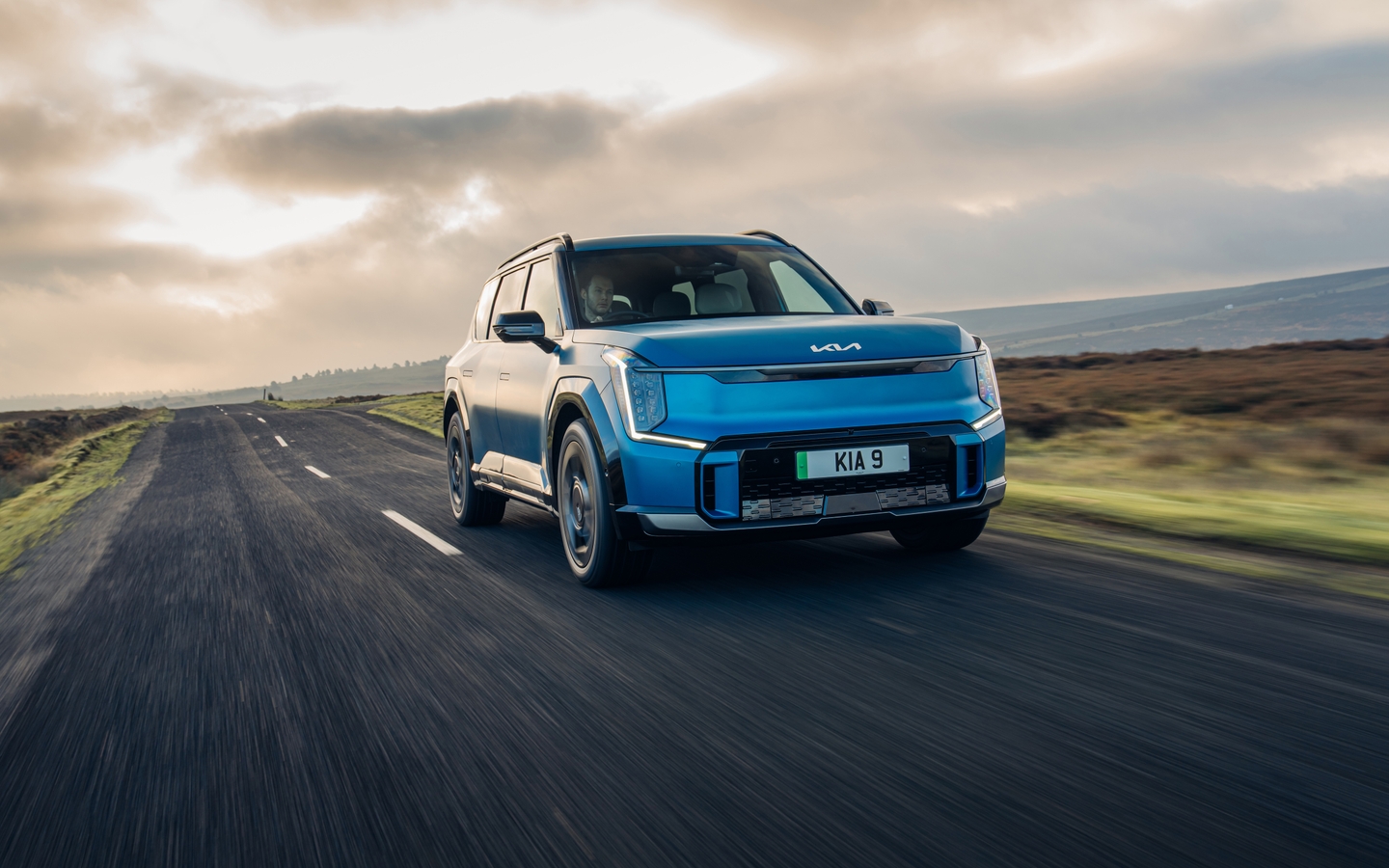 Blue Kia EV9 driving on a country road