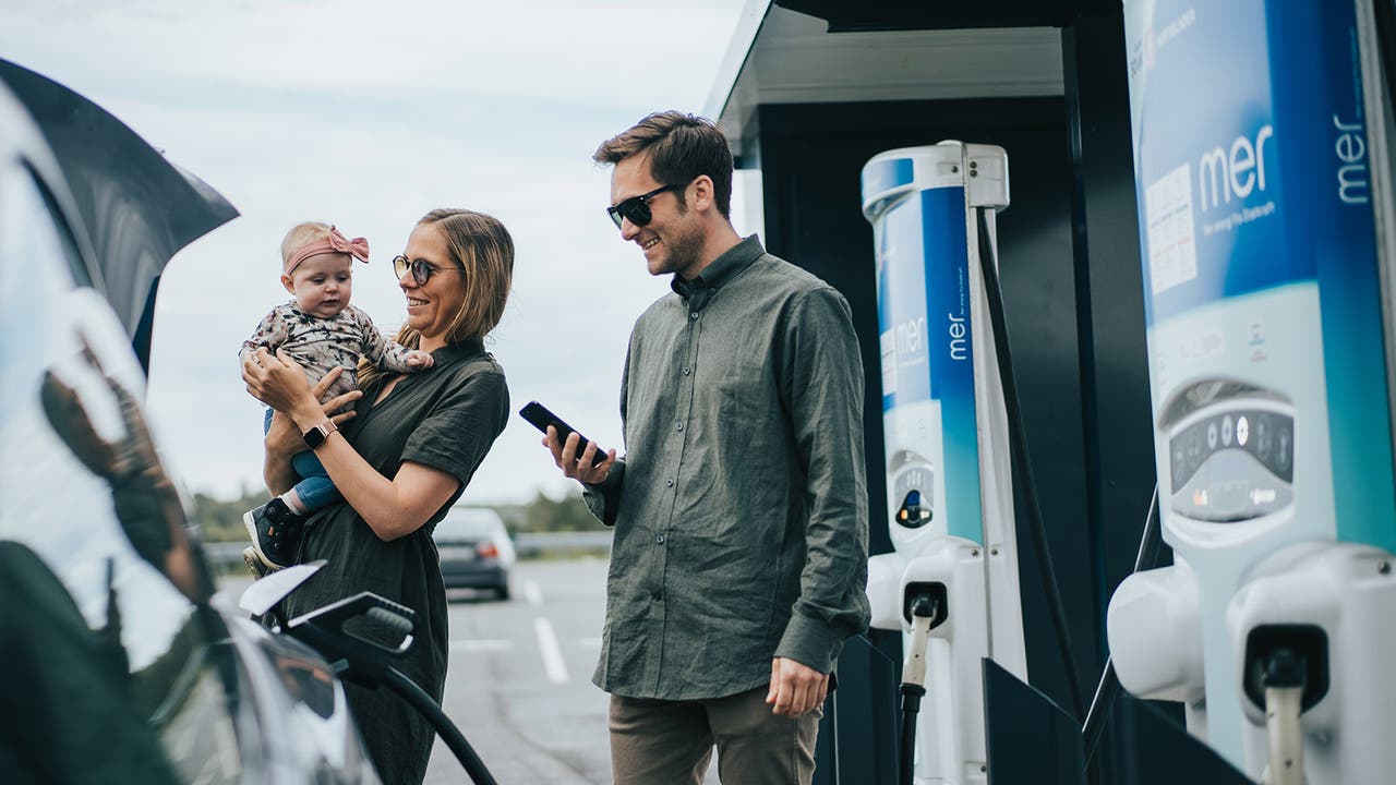 Smiling family with baby plugs their EV in to charge.