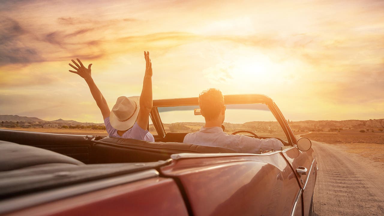 Drivers sit in a convertible with the sunset glaring ahead of them