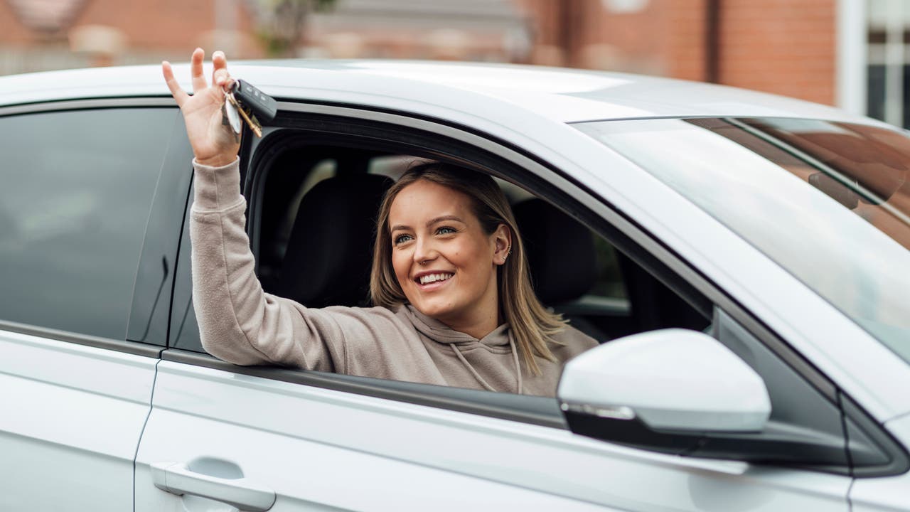 Smiling lady holding car keys out of a car window looking away from the camera