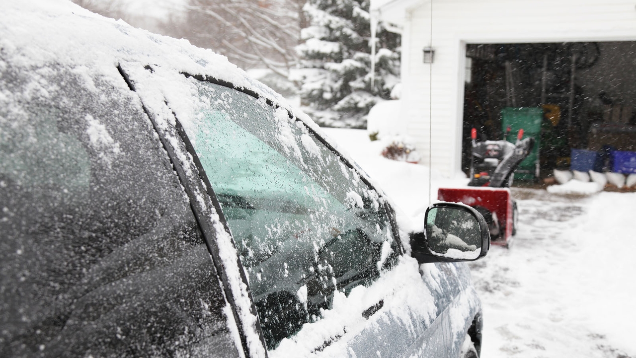 A frozen car in the foreground in front of an open garage