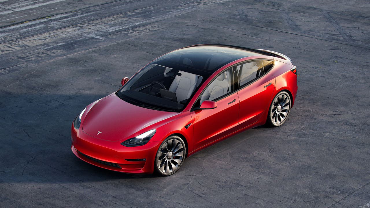 A red Tesla Model 3 parked on some Tarmac, three quarter shot from high up