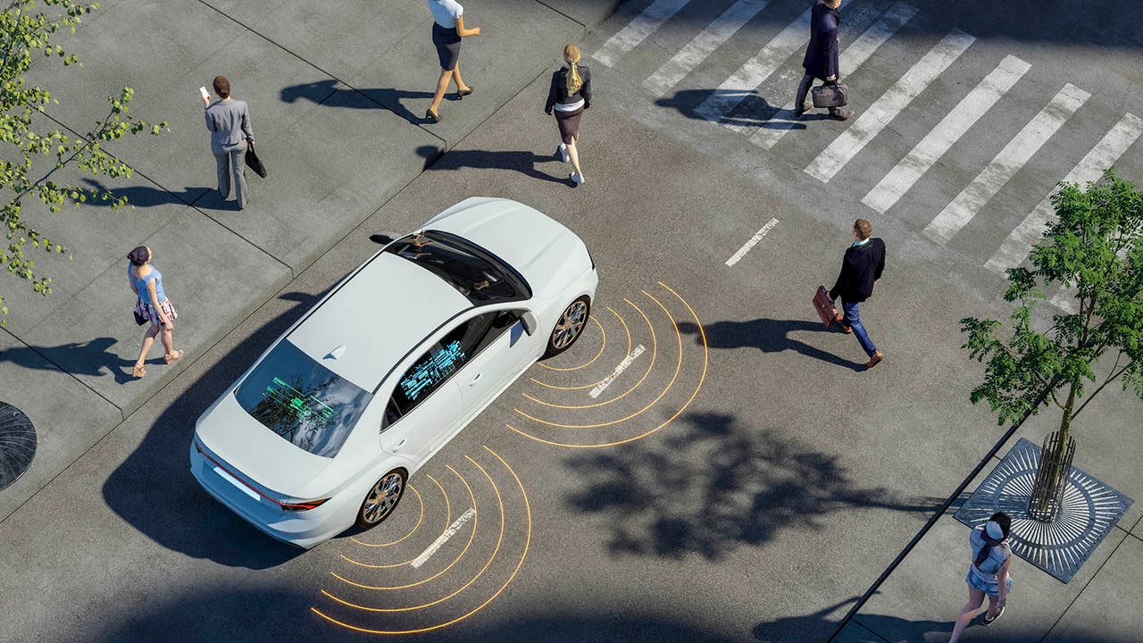 A white self-driving car navigates through a busy pedestrian crossing