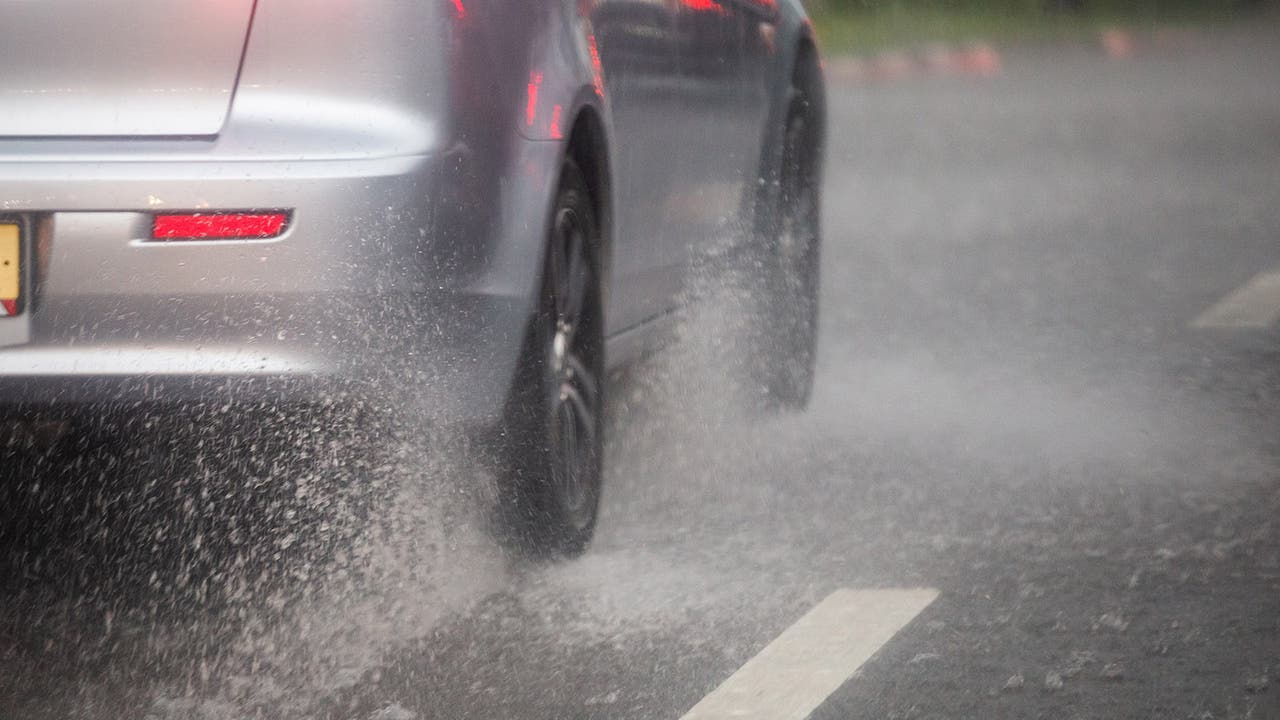 Silver car kicks up spray driving down a wet road