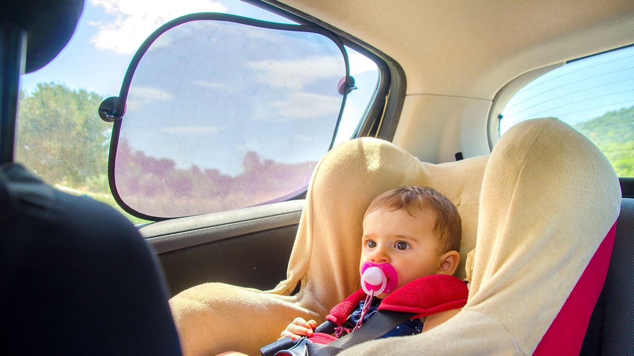 A baby looks placid in a car seat while a sunshade blocks out the sun's rays