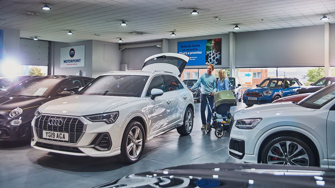 Parents with child in pushchair look into the boot of a white Audi Q3 at a Motorpoint store