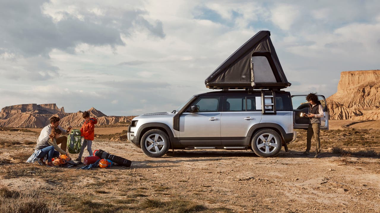 Family camping next to Land Rover Defender 110 with tent on the roof