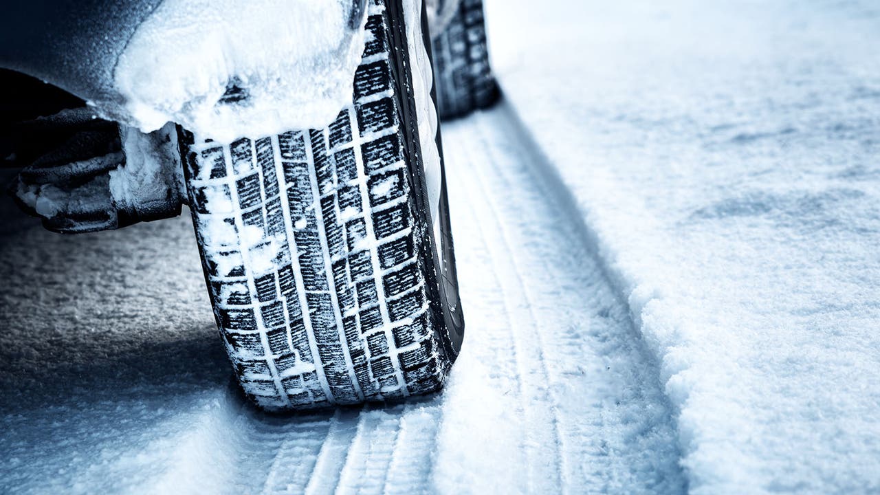 Dramatic shot of a snow-covered winter tyre driving through snow.