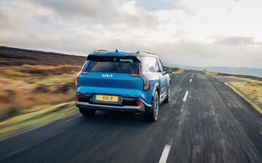 Blue Kia EV9 driving down a country road, viewed from behind