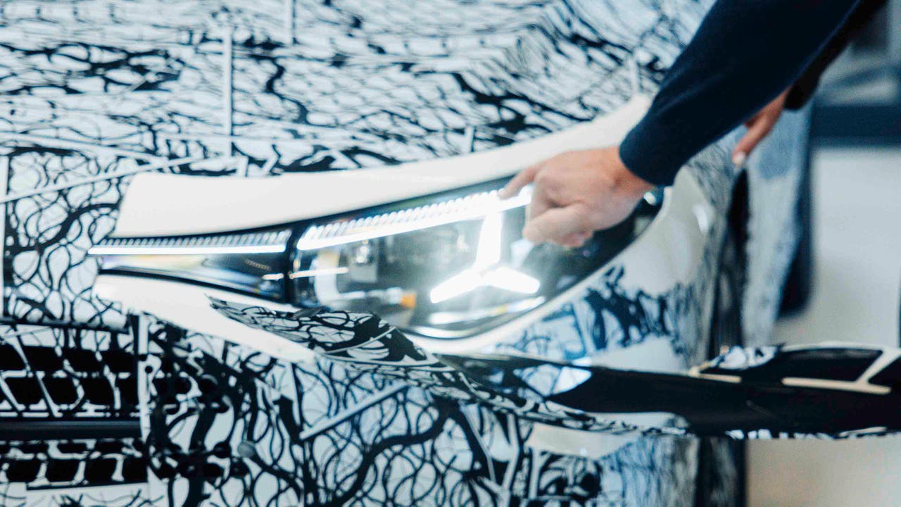 Mercedes CEO peeling off camouflage from the headlight of a new Mercedes CLA