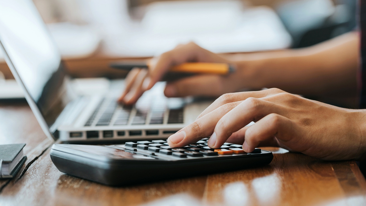 Person uses a laptop and a calculator on a desk