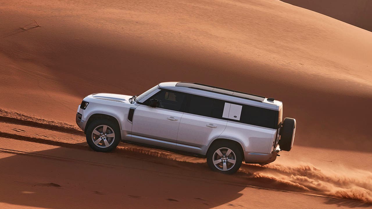 Land Rover Defender 130 in silver, driving through a sand dune