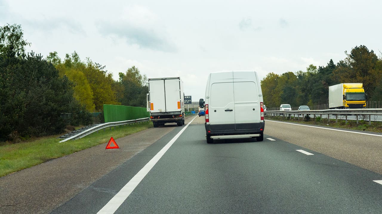 A motorway with traffic passing by a stopped lorry on the hard shoulder