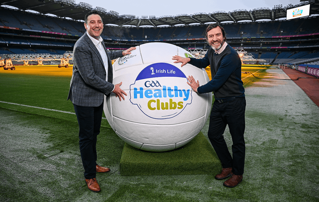 Two men and a giant football with the GAA Healthy Clubs logo