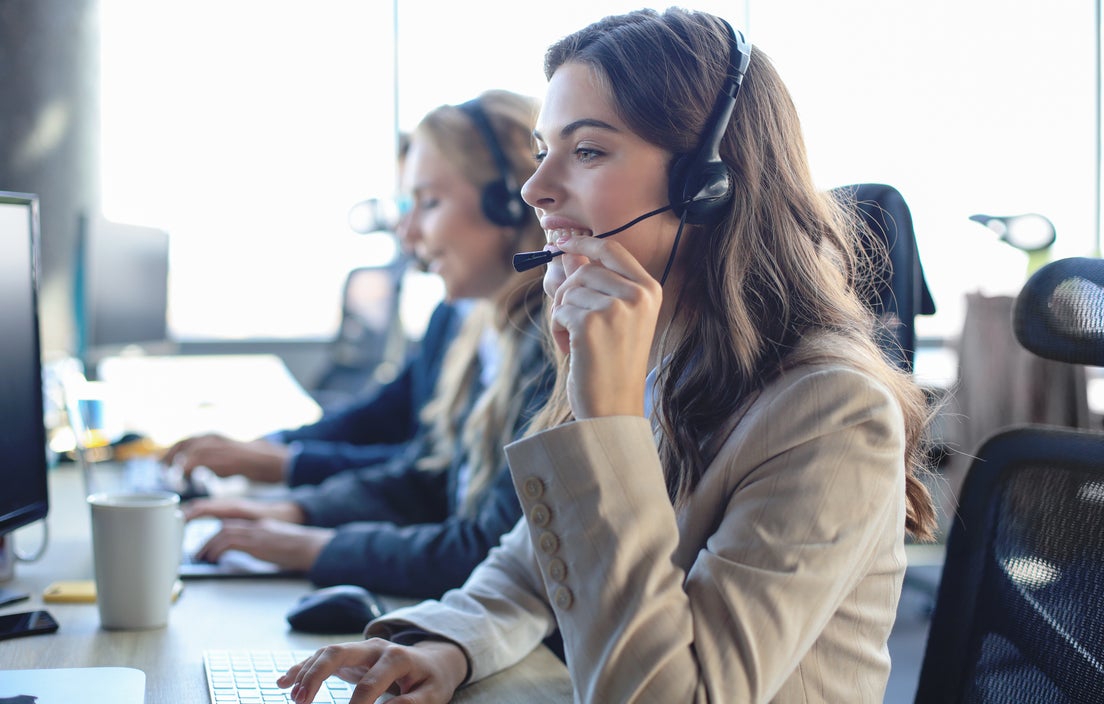 People wearing headsets working at desktop computers in an office environment.