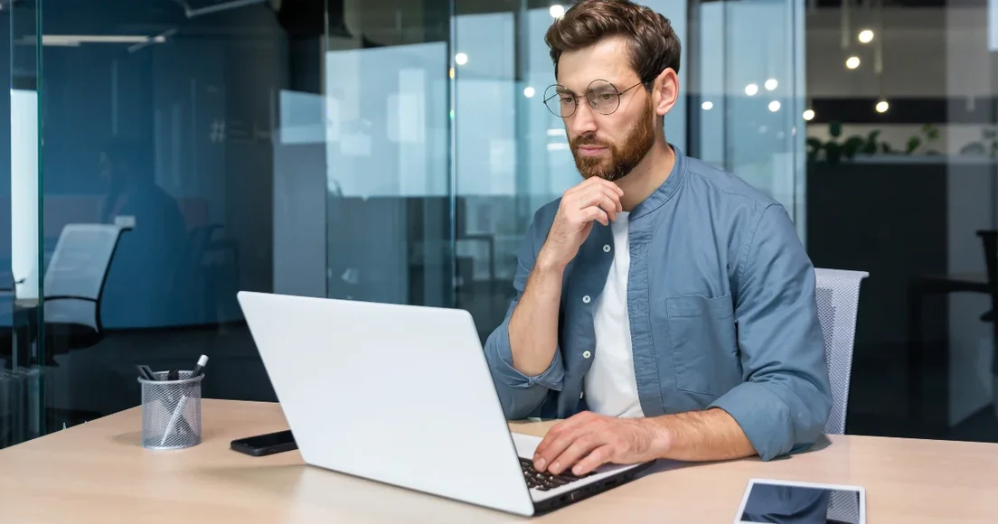 A man in a glass meeting room working on his laptop at a desk