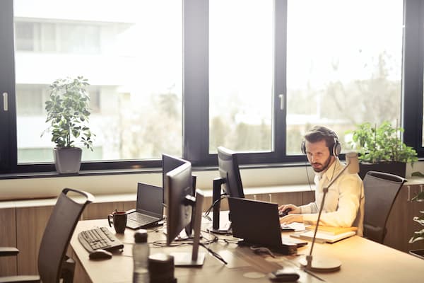 A man in an office at a desk and wearing a headset
